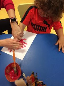 Toddler pressing hand with red paint on to paper