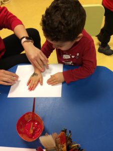 Kid pressing hand on white paper with red paint