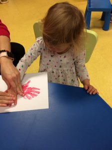 Toddler pressing hand with red paint on to paper twice