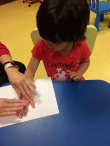 Toddler pressing hand with red paint on to paper wearing a red shirt