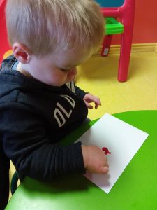 Toddler putting red paint on a piece of paper