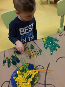 Kid colouring in hands with teal and yellow paint