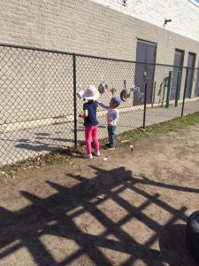 Two toddlers playing with kitchen equipment on a chain fence