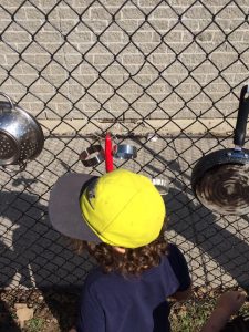Toddler with a yellow hat playing with kitchen equipment on a chain fence