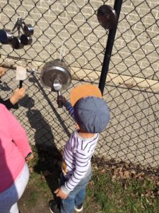 Toddler playing with kitchen equipment on a chain fence and having the time of his life
