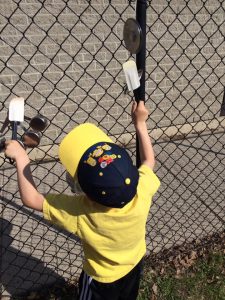 Toddler playing with kitchen equipment on a chain fence