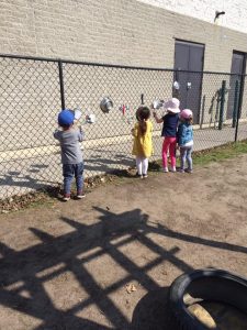 Several toddlers playing with kitchen equipment on a chain fence