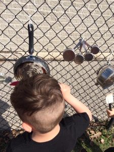 Toddler playing with a pot connected to a chain fence
