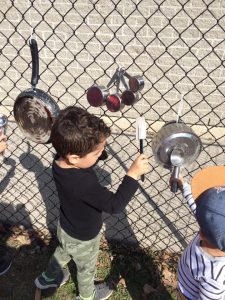 Toddlers playing with spatula's and other kitchen equipment attached to a chain fence