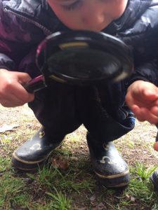 Toddler holding magnifying glass to soil
