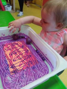 Toddler rolling around marbels in paint