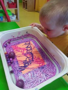 Toddler looking at colourful marbles rolled around in purple paint