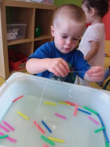 Kid playing with thin string and connecting colourful pieces together