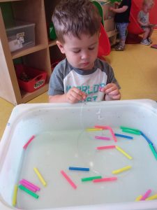 Toddler starring at string, looking to see what colourful pieces to add