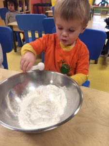 Kid adding dry ingredients to a bowl