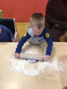 Kid rolling dough on a wood table