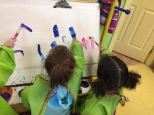 Kids doing their first stroke of paint on a canvas