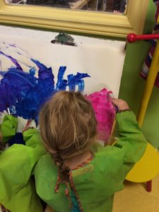 Toddler painting pink on a canvas