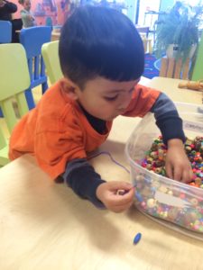 Little kid politely taking beads from a bead bin