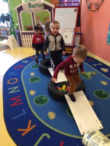 Kids having an obstacle course on a blue rug in a classroom