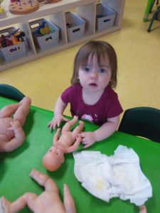 Kid starring at a camera with a baby doll on a table