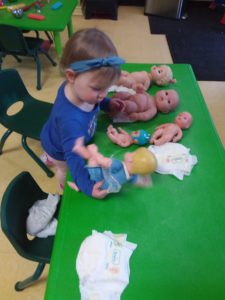 Toddler playing with some baby dolls on a green table