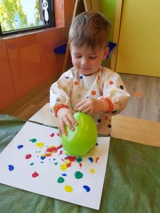Toddler rubbing a balloon on paint that's on white paper