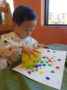 Toddler rubbing a yellow balloon on white paper that has paint on it