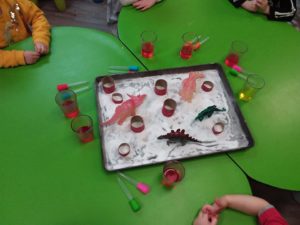 Toy dinosaurs with glasses full of coloured water