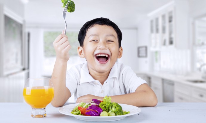 A child holds up a piece of broccolli
