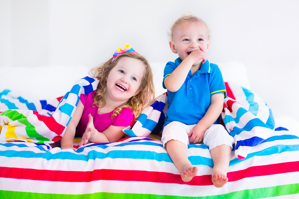 A toddler and older child sit on a bed