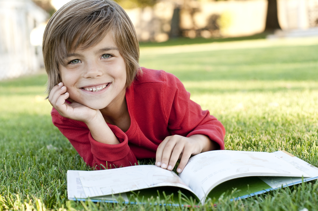 A young boy reads a book in a park