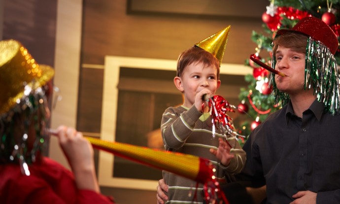 Parents and their child wear party hats and blow into party horns in their living room.