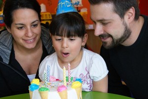 A girl blows out birthday candles with her parents