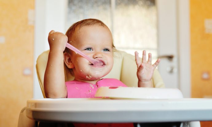 A baby holds a spoon in her highchair