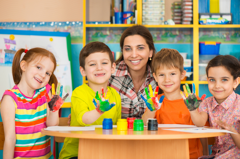 A daycare owner fingerpaints with students