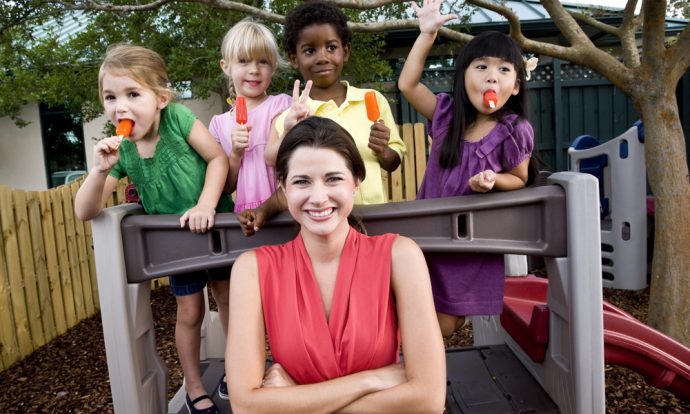 A happy and confident woman stands in front of a group of children.