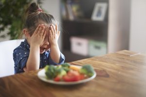 A child covers her eyes to a plate of vegetables
