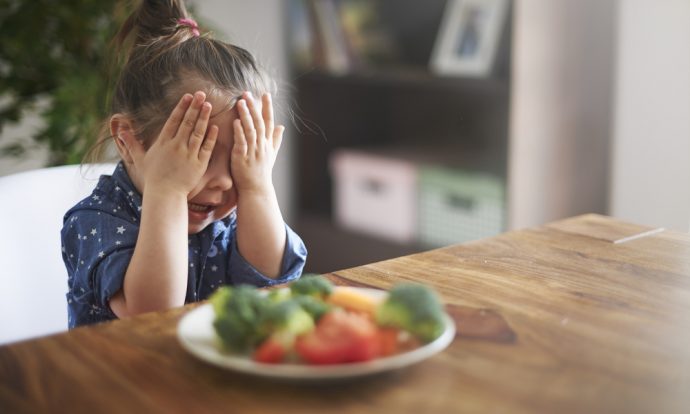 A child covers her eyes to a plate of vegetables